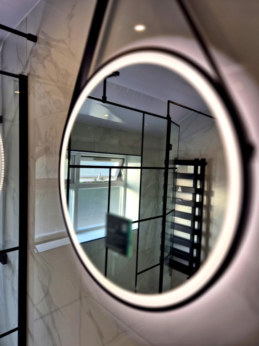 Round hanging mirror reflecting black-frame shower enclosure